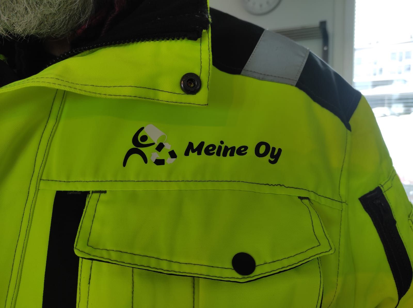 Helposti näkyvä keltainen takki, jossa yrityksen logo