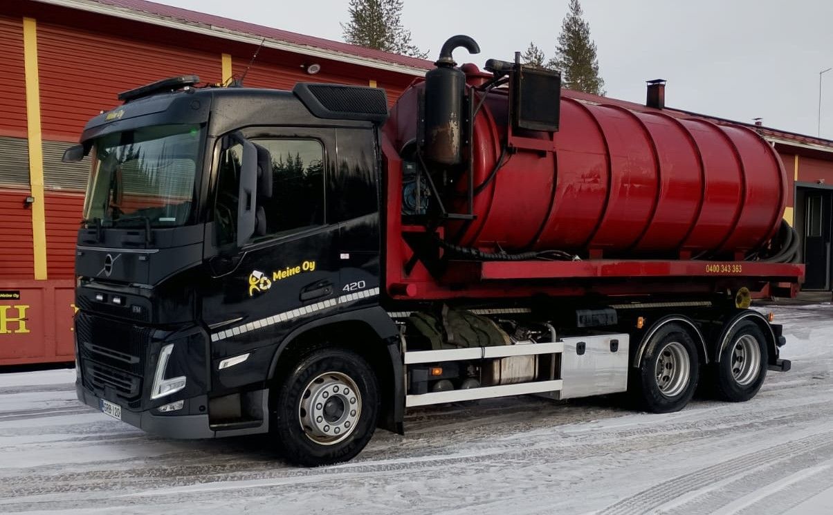 Musta ja punainen imuriauto lumisella maalla punaisen rakennuksen edessä.