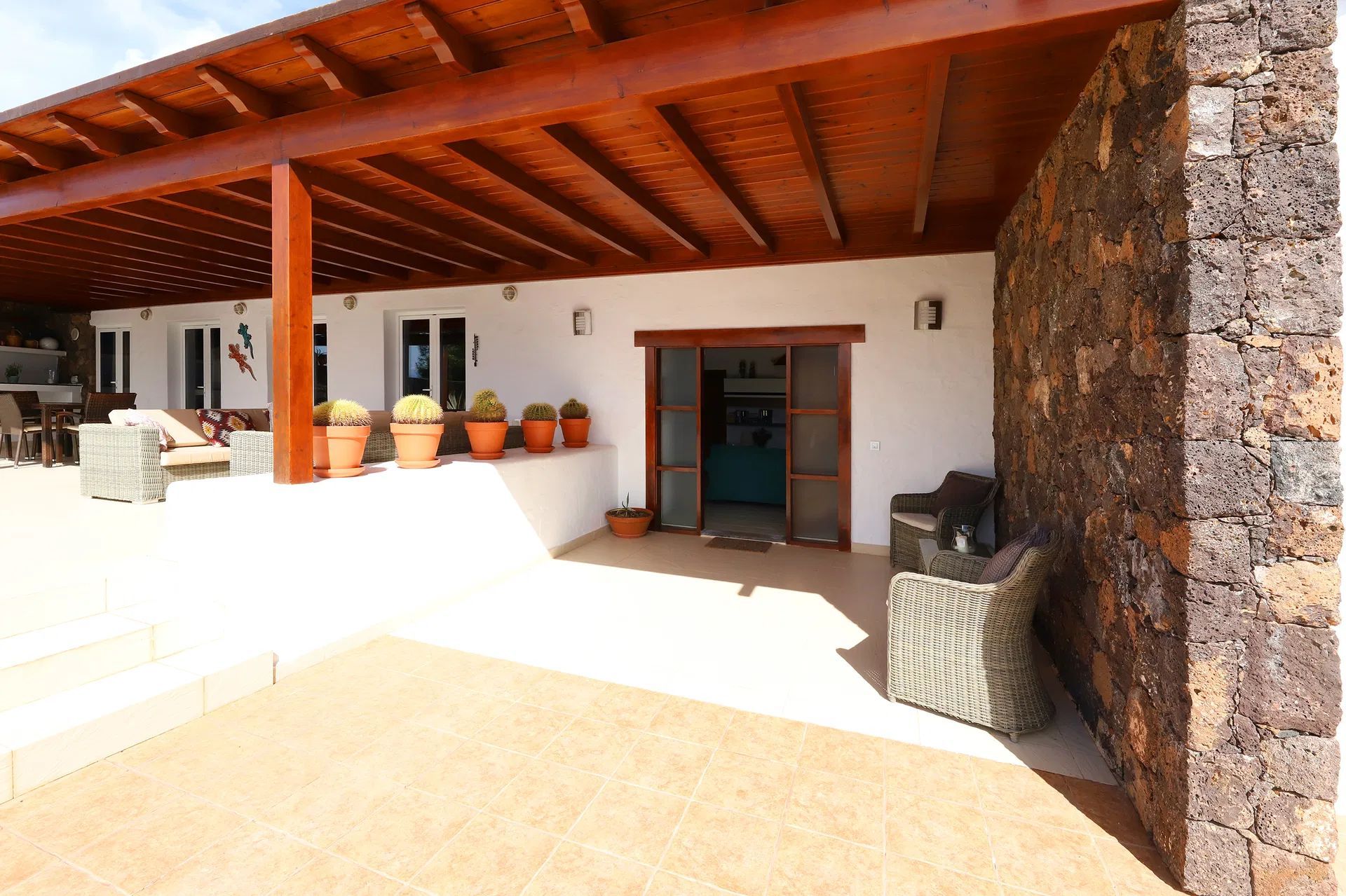 Covered patio entrance with dark wood beams and a volcanic rock wall. Villa Salvo | Los Mojones | Puerto del Carmen | Lanzarote.