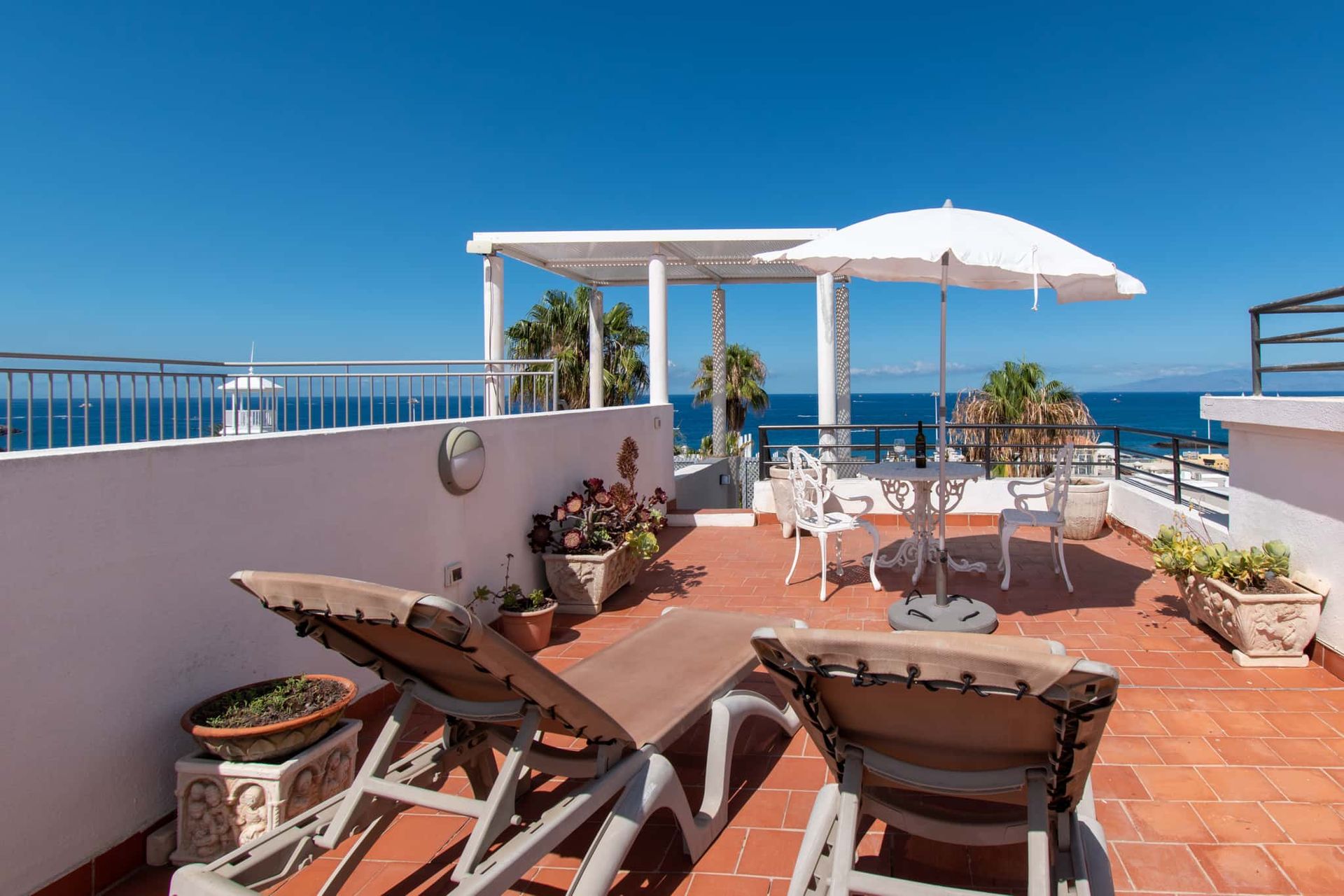 Roof terrace with sun loungers, patio table and chairs with sun umbrella and sea views.