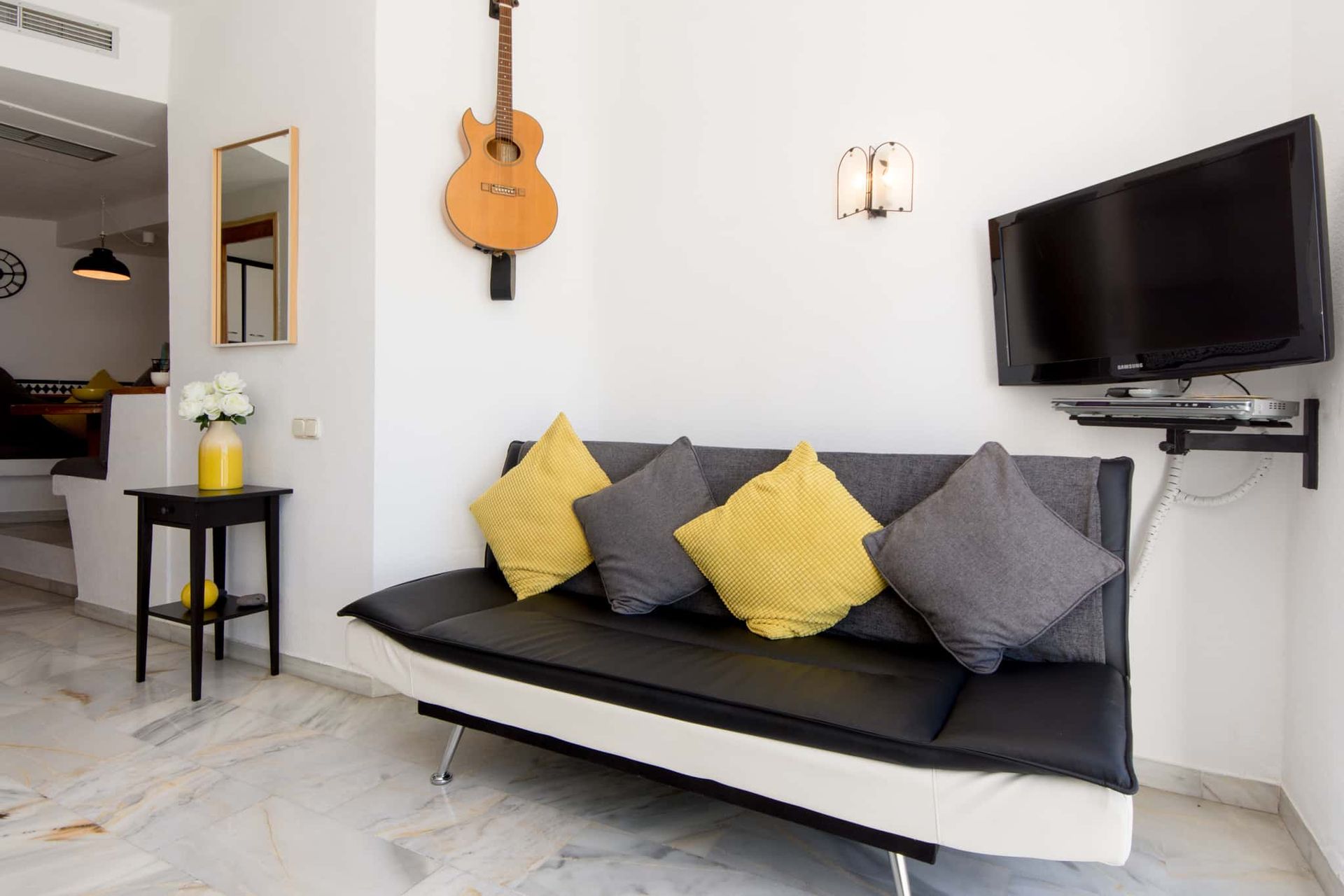A living room with a couch , television and a guitar hanging on the wall.
