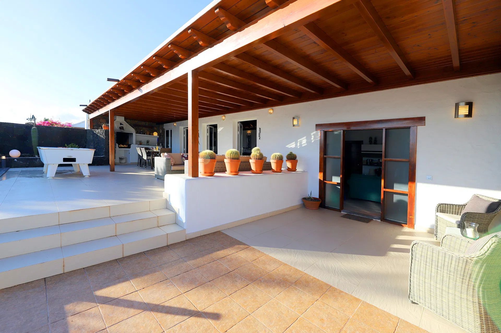 Patio with white walls, wooden pergola, potted cacti, and steps to a sunny area. Villa Salvo | Los Mojones | Puerto del Carmen | Lanzarote.