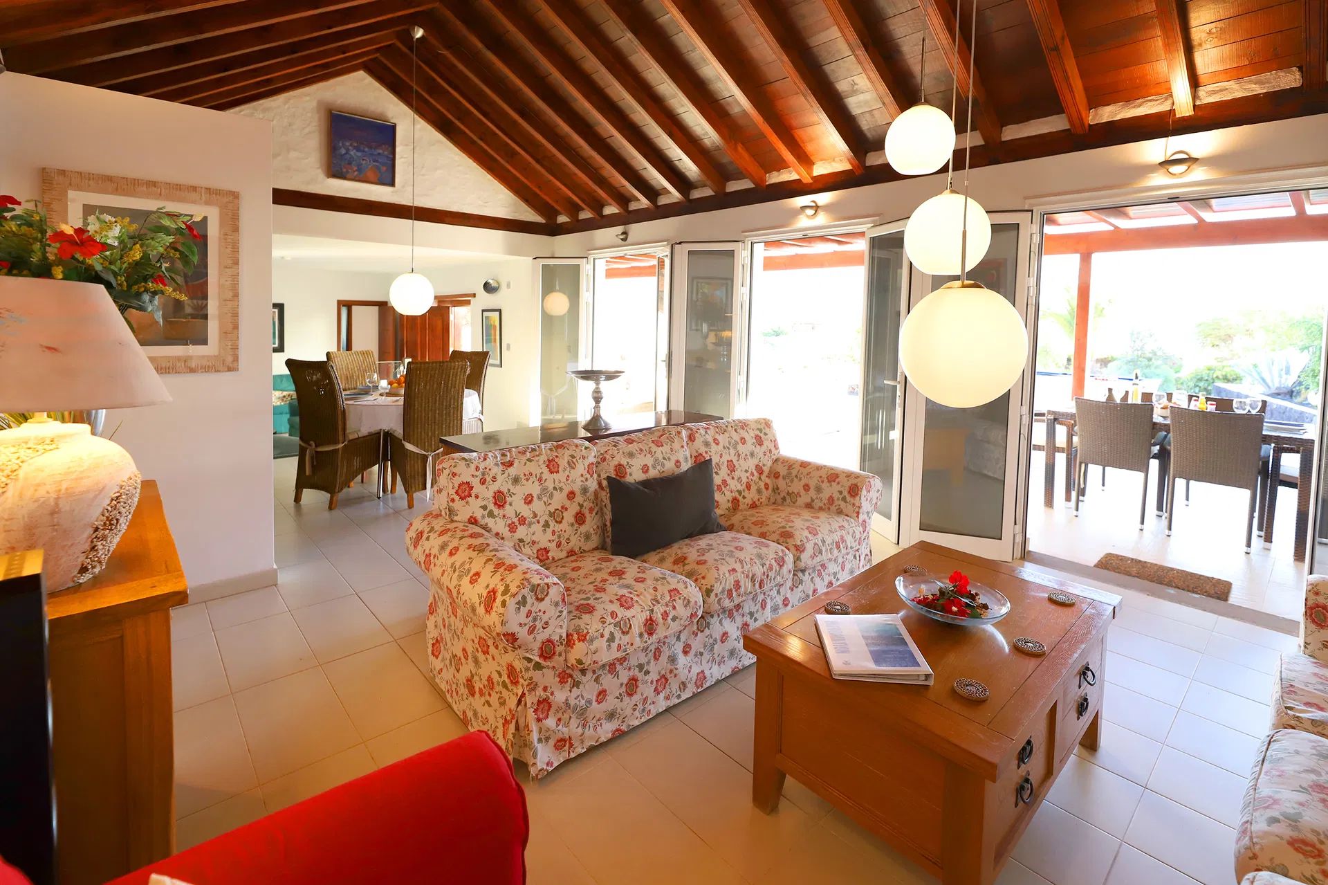 Living room with floral sofa, wooden coffee table, and open doors to a dining area. Villa Salvo | Los Mojones | Puerto del Carmen | Lanzarote.
