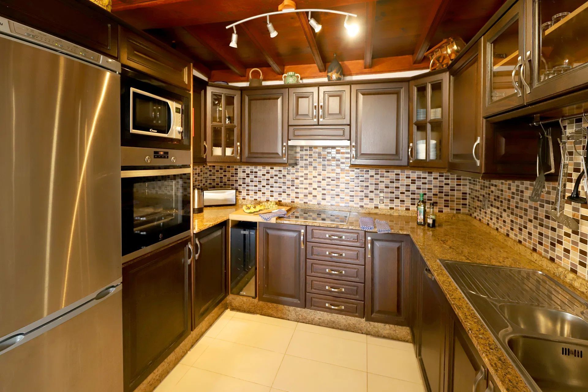 A brown kitchen with stainless steel appliances, granite countertops, and mosaic backsplash. Villa Salvo | Los Mojones | Puerto del Carmen | Lanzarote.