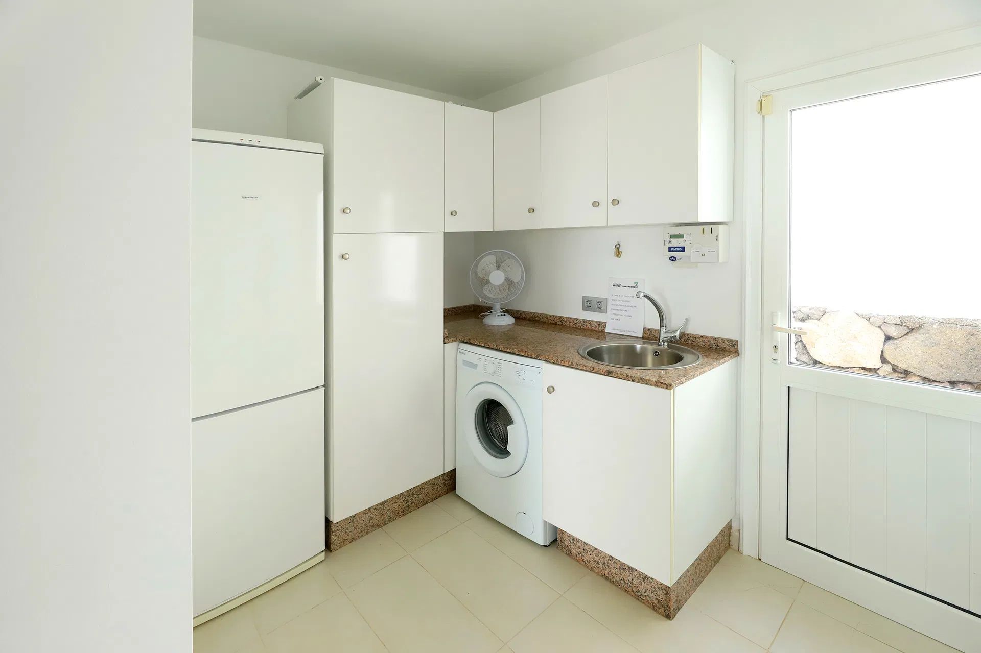 White laundry room with cabinets, refrigerator, washing machine, and sink. Window lets in light. Villa Salvo | Los Mojones | Puerto del Carmen | Lanzarote.