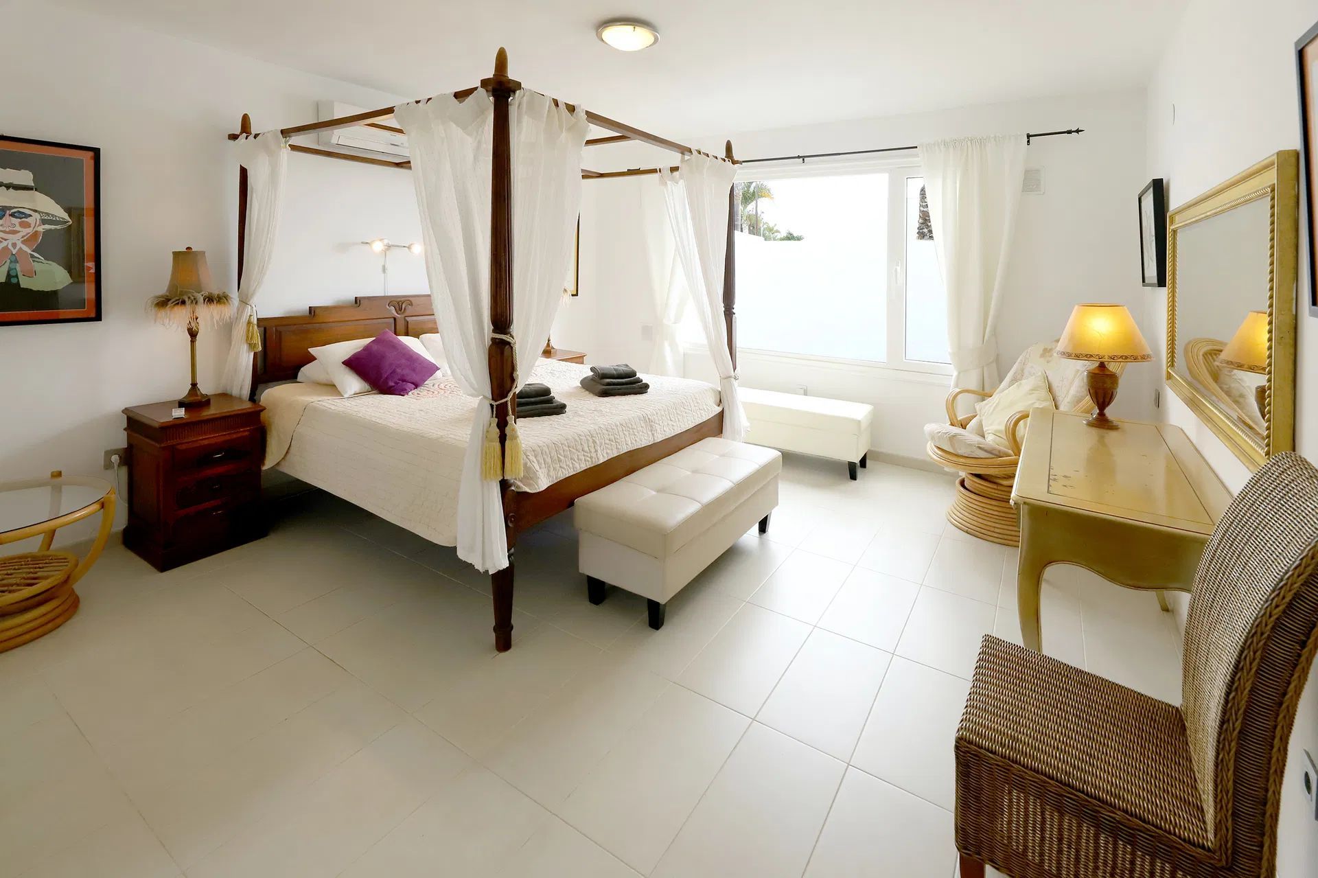 Bedroom with canopy bed, white walls, natural light, and wicker chair. Villa Salvo | Los Mojones | Puerto del Carmen | Lanzarote.