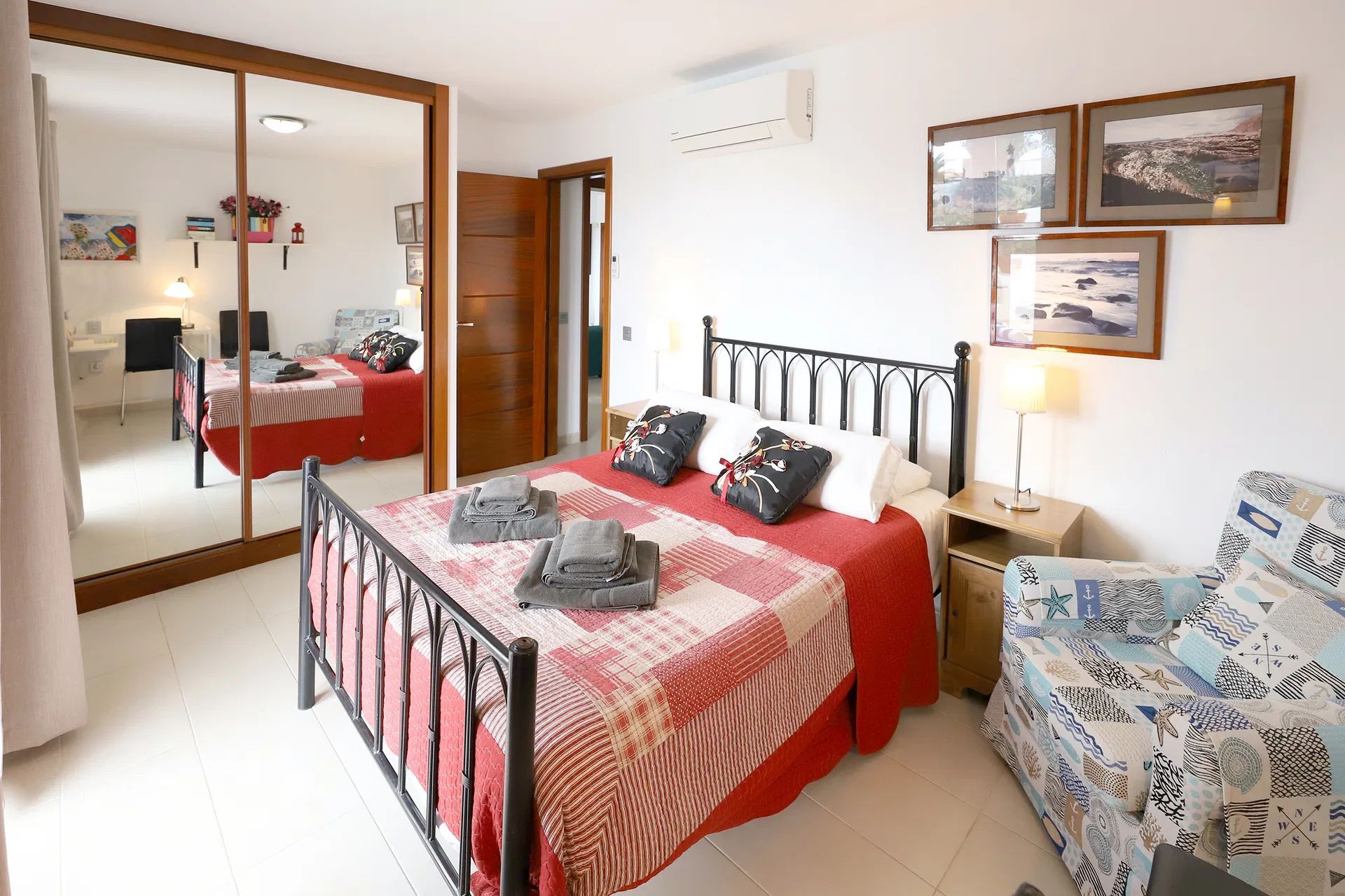 Bedroom with a double bed, red and white quilt, framed art, and a mirrored closet. Villa Salvo | Los Mojones | Puerto del Carmen | Lanzarote.