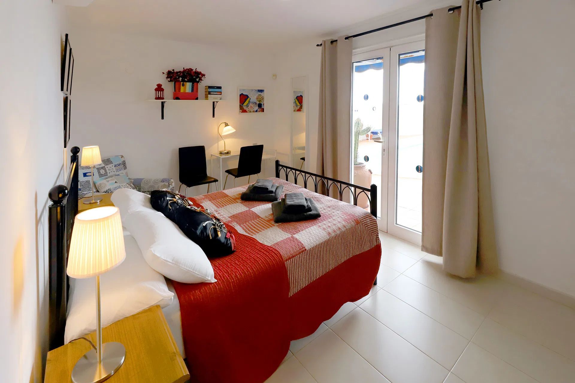 Bedroom with a bed, table, and chairs; red, white, and black colors; window with curtains.