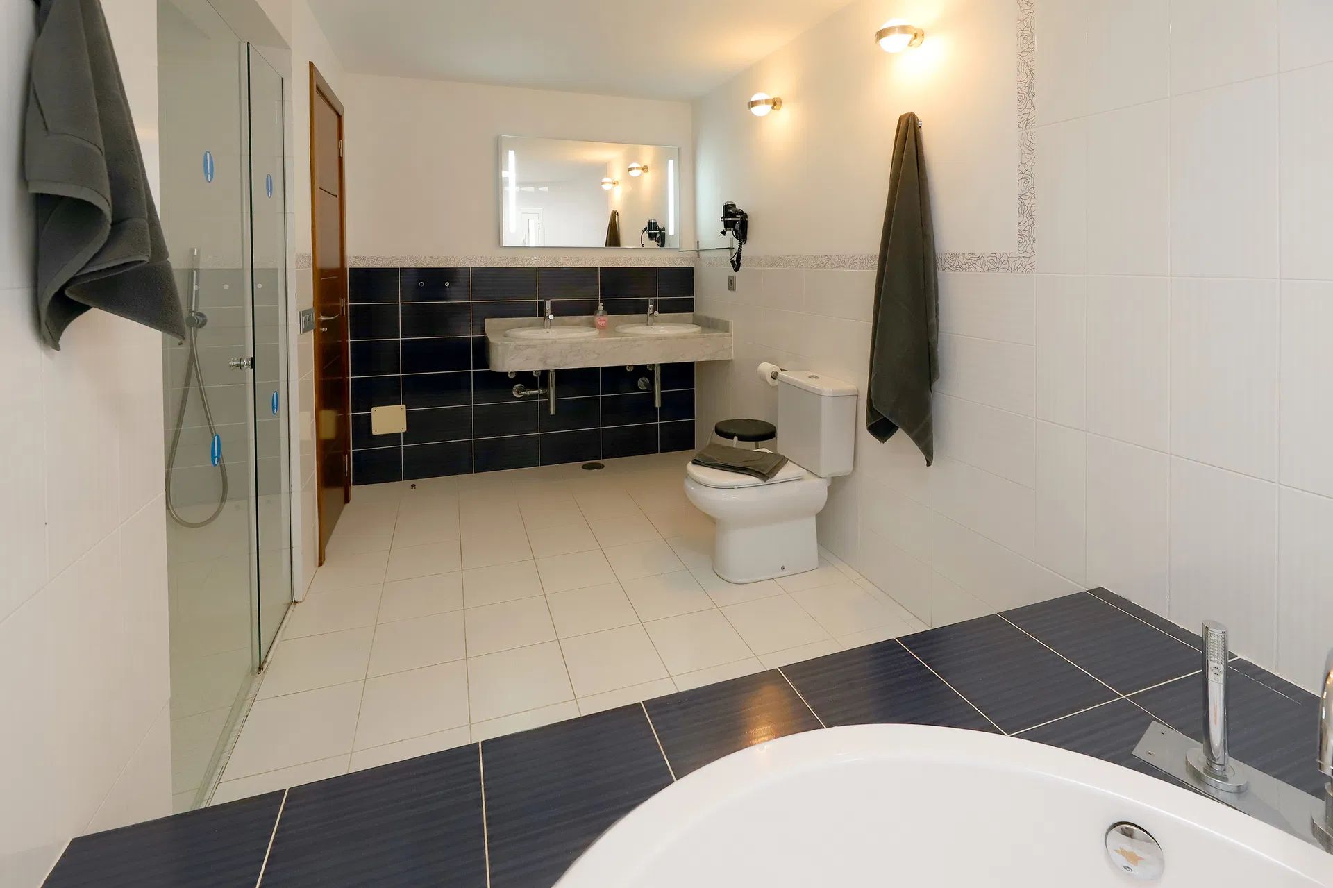 Spacious white bathroom with a blue tiled accent wall, bathtub, and walk-in shower. Villa Salvo | Los Mojones | Puerto del Carmen | Lanzarote.
