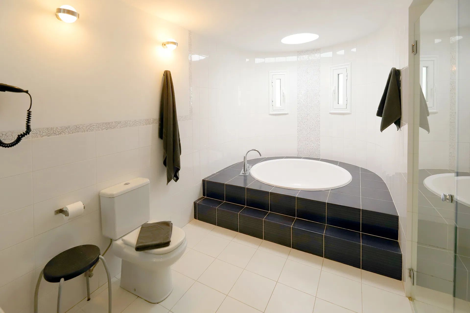 White bathroom with a round tub on a raised platform, toilet, stool, and towel. Villa Salvo | Los Mojones | Puerto del Carmen | Lanzarote.
