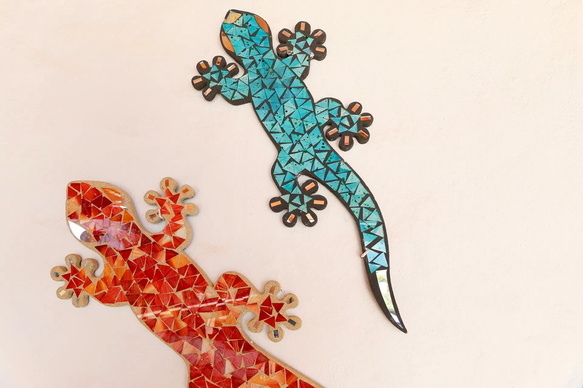Two mosaic geckos, one blue, one red, on a white wall. Villa Salvo | Los Mojones | Puerto del Carmen | Lanzarote.