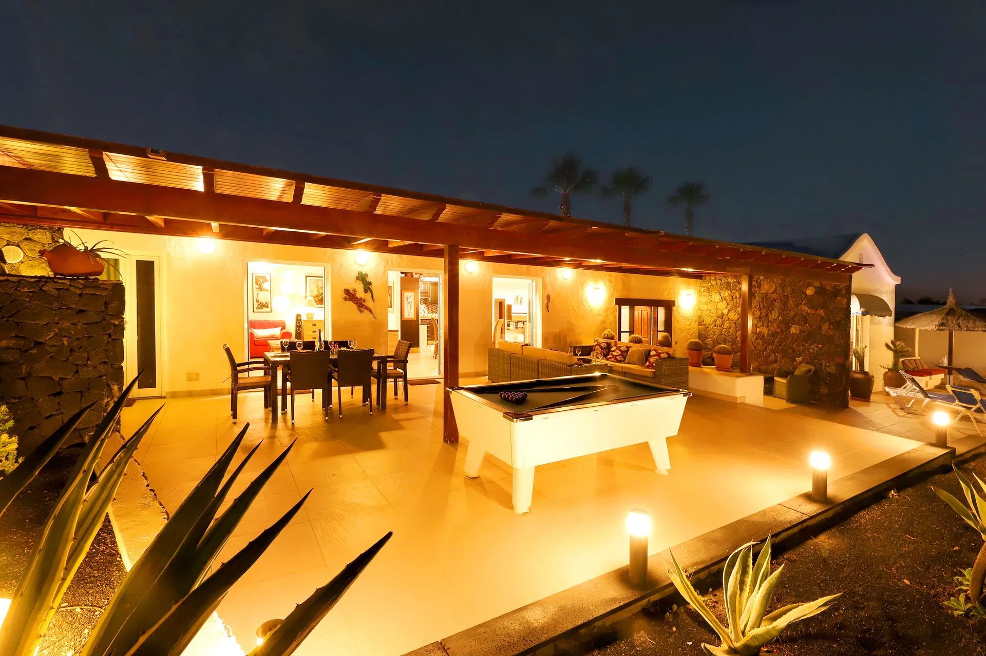 Night-time patio with illuminated pool table, dining table, and seating area. Villa Salvo | Los Mojones | Puerto del Carmen | Lanzarote.