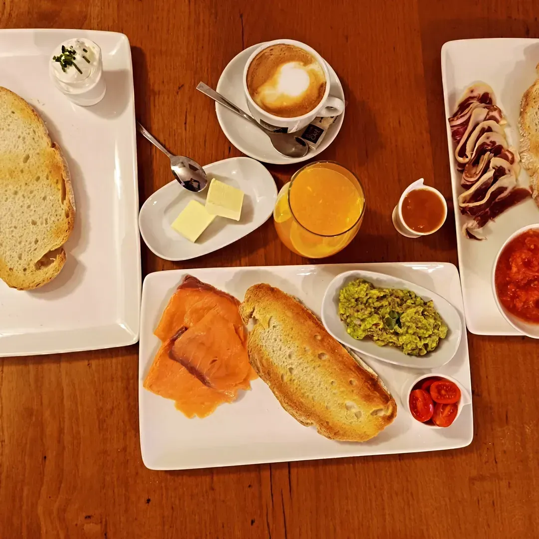 Gosaria egurrezko mahai batean zabalduta: tostadak, izokina, aguakatea, hirugiharra, tomatea, kafea, zukua.