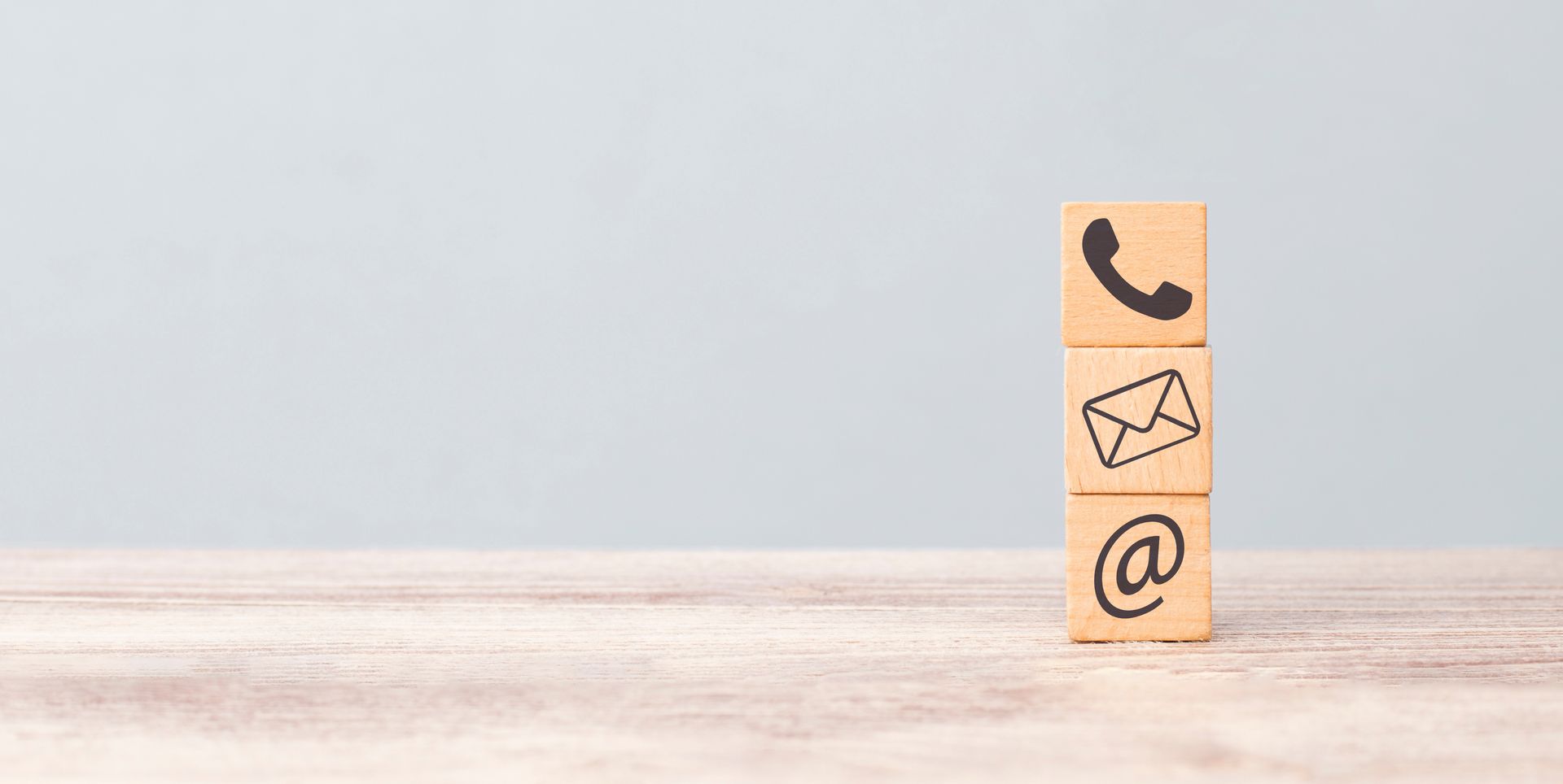 Ein Holzblock mit einem Telefon, einem Umschlag und einem @-Zeichen darauf
