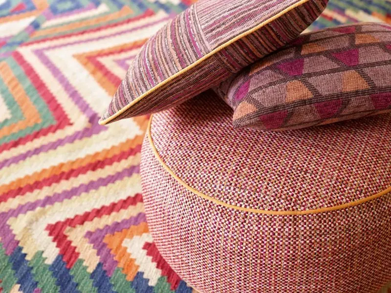 Zwei Kissen liegen auf einem rosafarbenen Ottomanen auf einem bunten Teppich