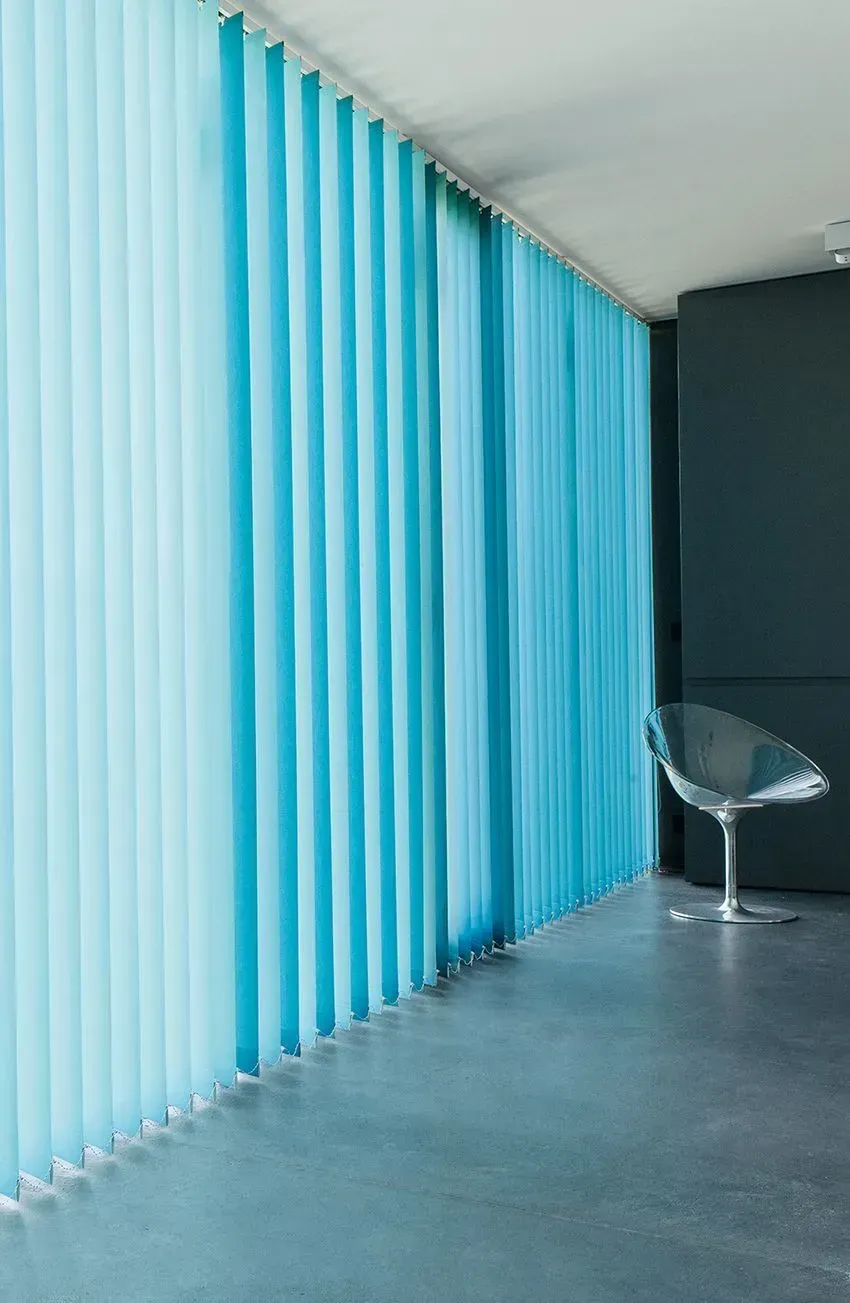 Ein Stuhl steht vor einem Fenster mit blauen Vertikaljalousien