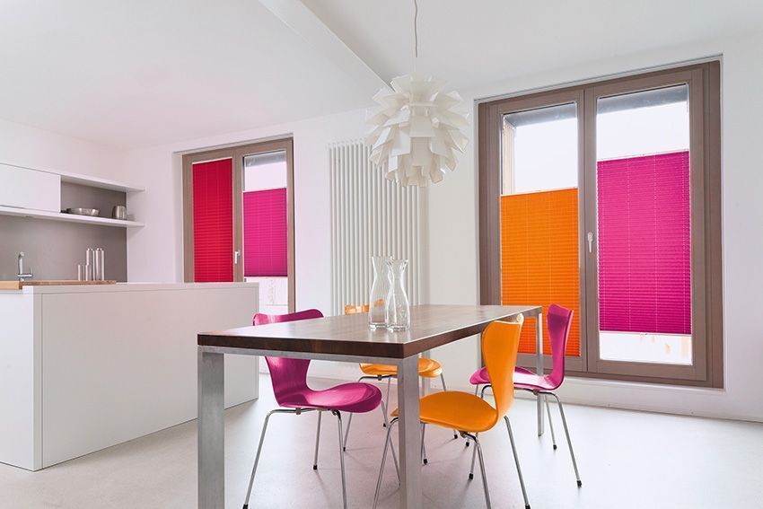 Ein Esszimmer mit Tisch und Stühlen und rosa und orangefarbenen Jalousien