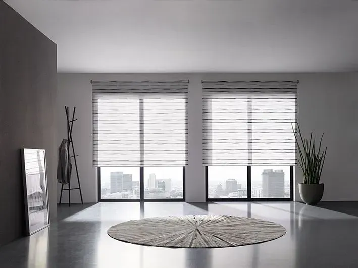 Ein Wohnzimmer mit einem runden Teppich, Jalousien und einem Spiegel