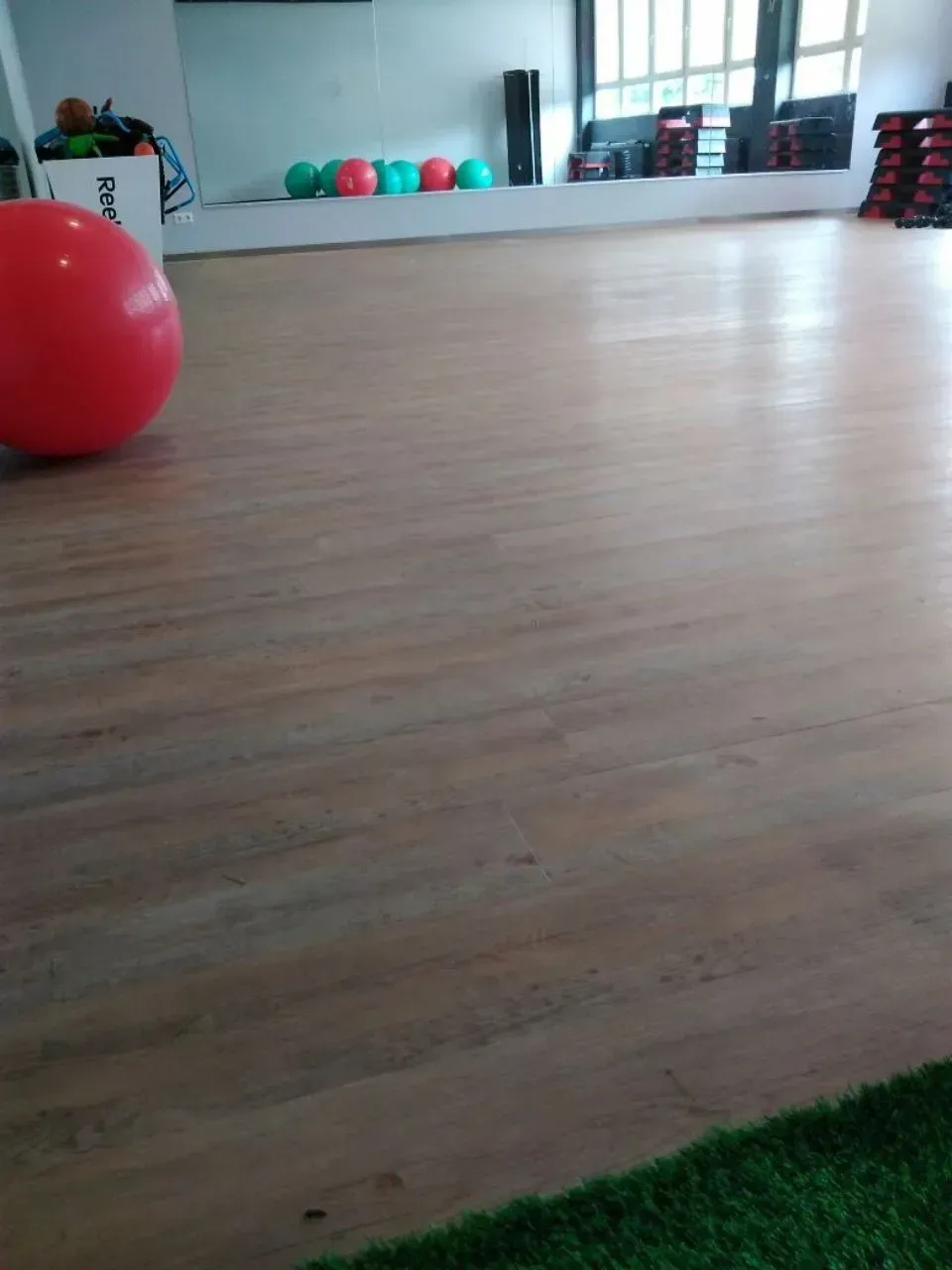 Ein großer roter Ball liegt auf einem Holzboden in einer Turnhalle