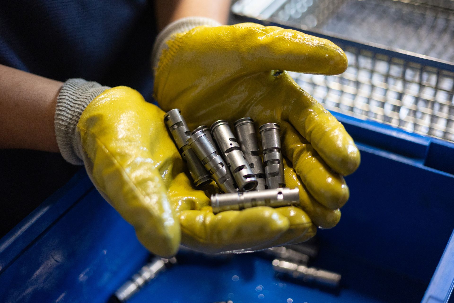 Mitarbeiter hält Metallteile nach dem Härtungsprozess zur Kontrolle in den Händen.