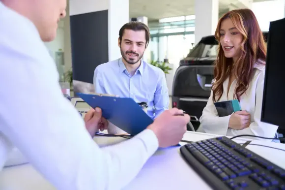 Una pareja revisa documentos con un vendedor en un escritorio en un concesionario de automóviles.