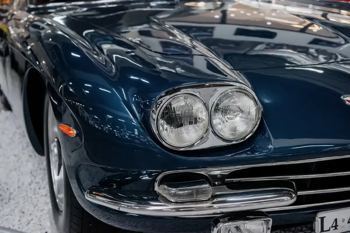 Parte frontal de un coche clásico de color azul, con faros y parrilla cromados.