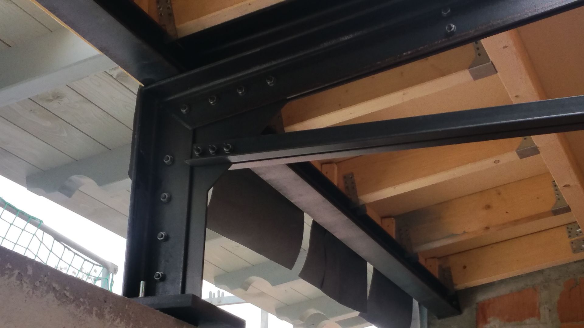 Schwarze Stahlträgerkonstruktion, die einen Holzboden mit einem daran hängenden Kabel in einer Baustellenumgebung stützt
