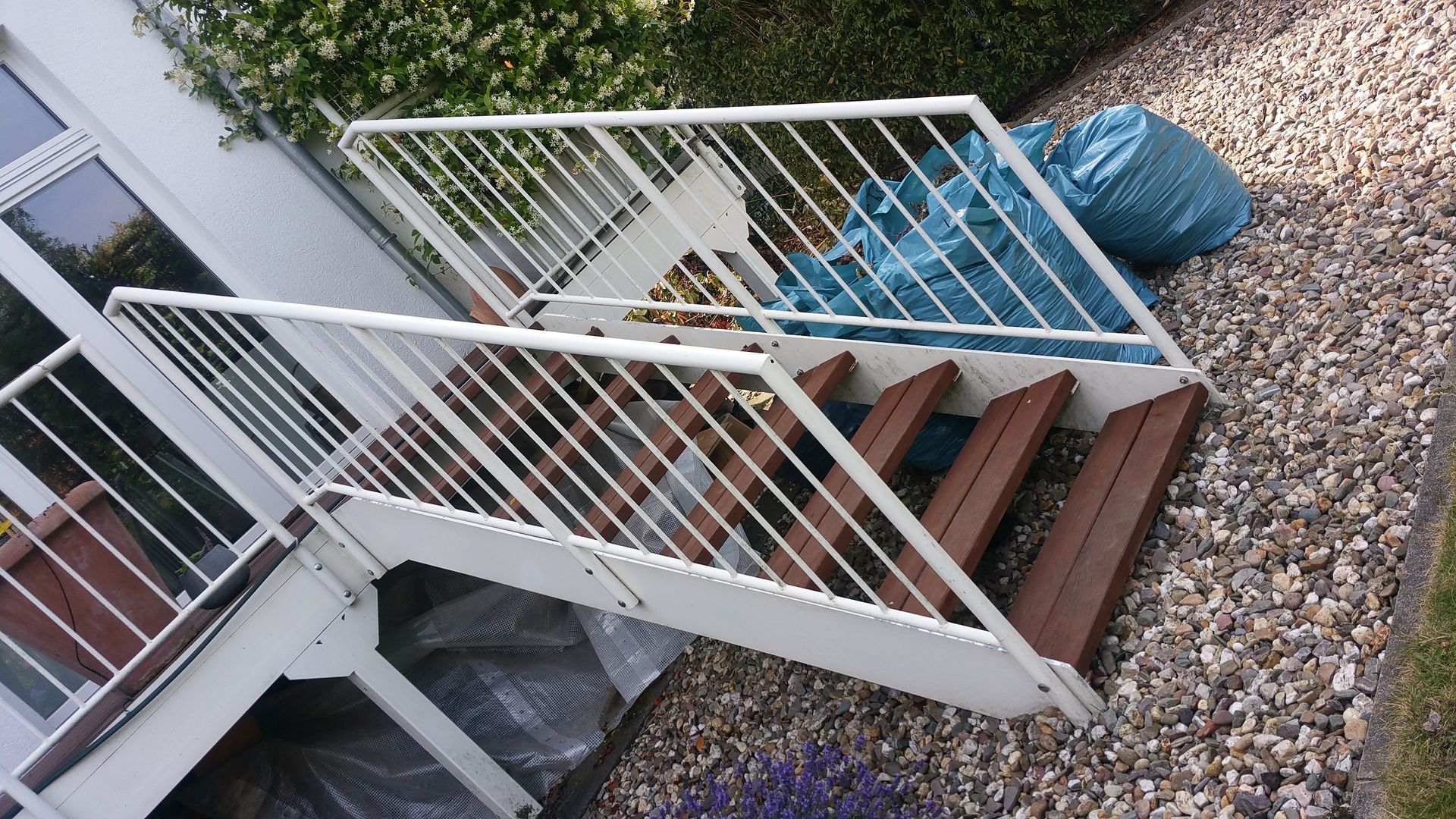 Außentreppe mit weißem Geländer neben einem Kieshof und mit blauen Planen abgedeckten Gegenständen