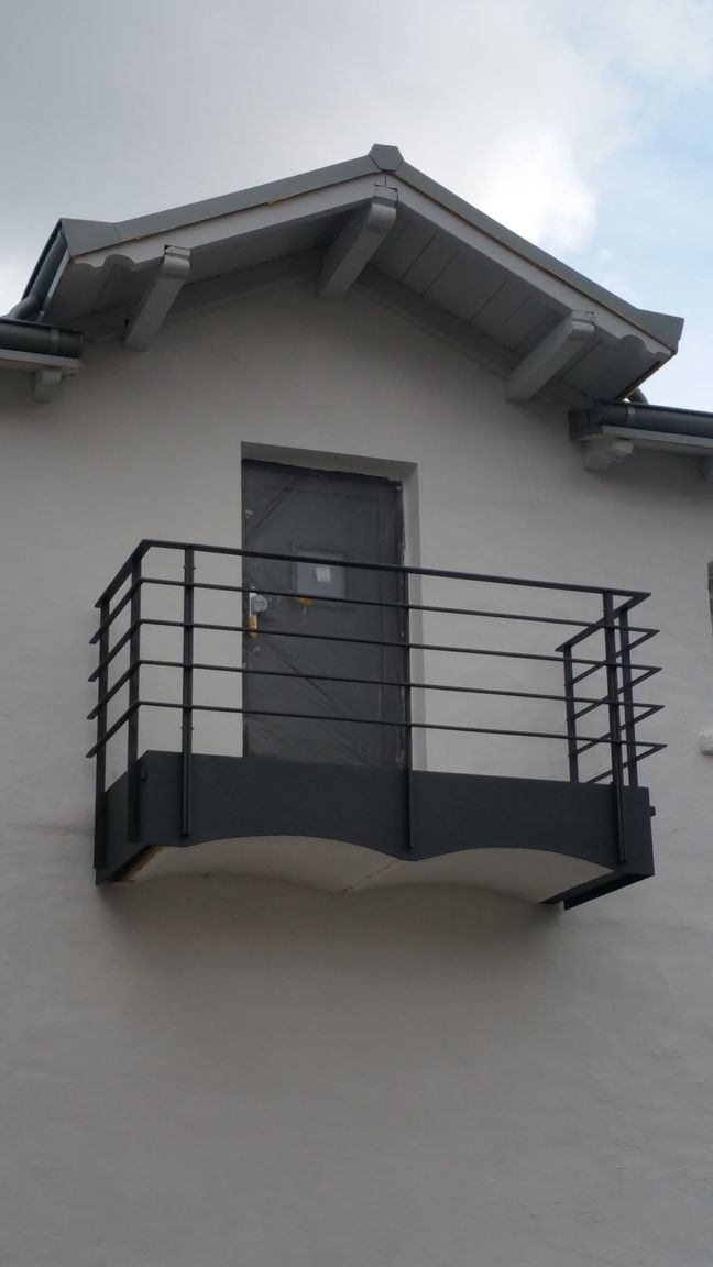 Kleiner, schwarzgeländerter Balkon unter einem Fenster an der weißen Hausfassade