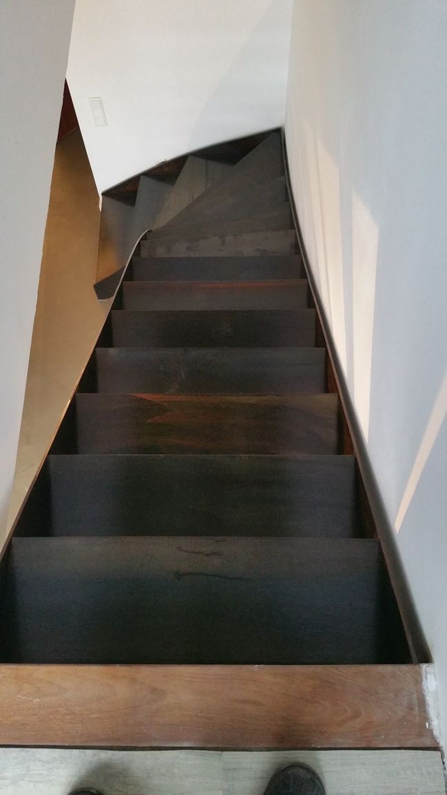 Schmale, dunkle Treppe mit weißen Wänden, die nach oben ins Innere führt.