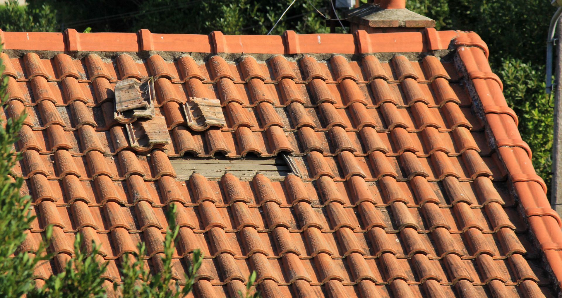 Toiture en tuiles rouges avec une section de tuiles manquantes et cassées.