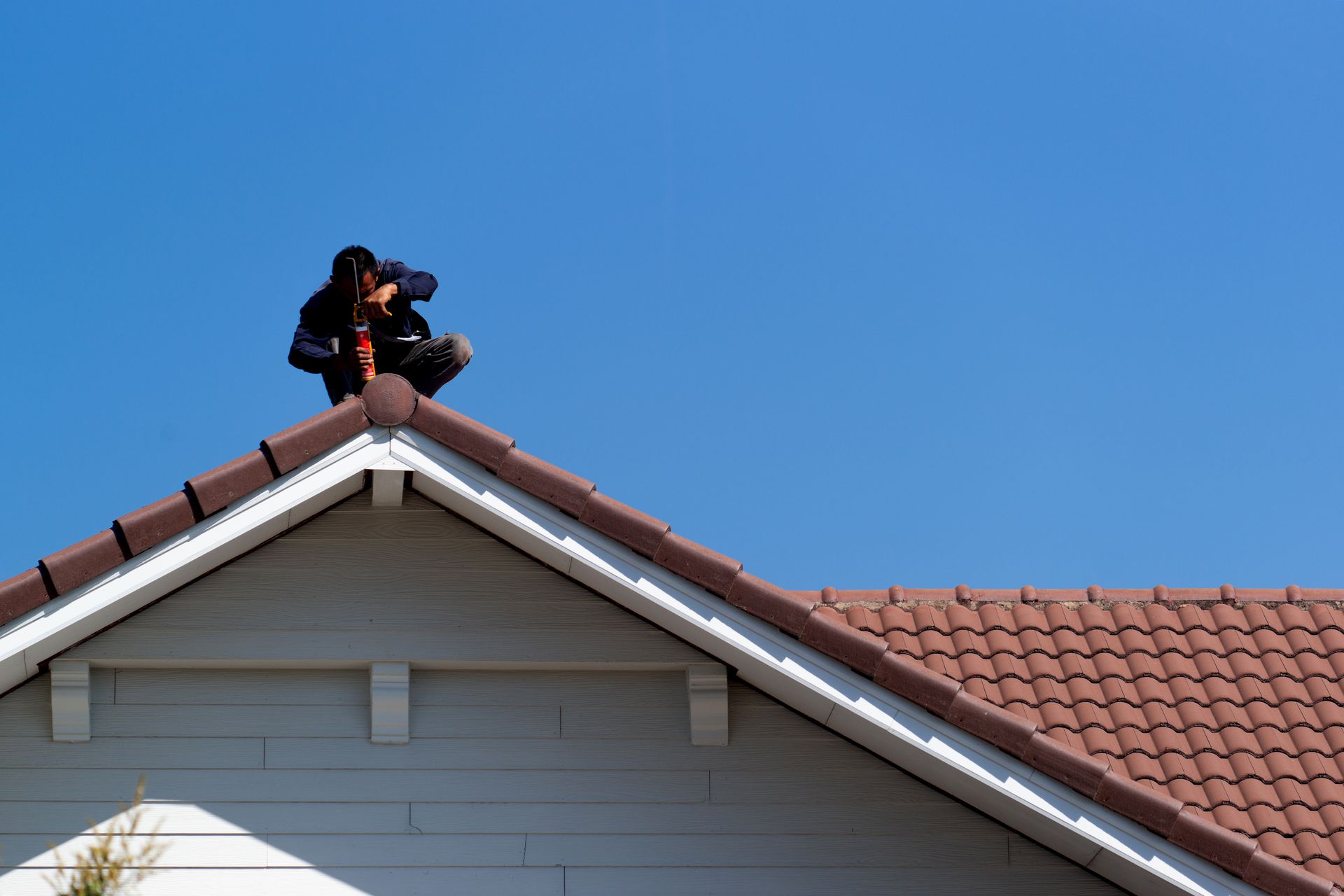 Une personne sur un toit, perceuse en marche. Ciel bleu en arrière-plan.