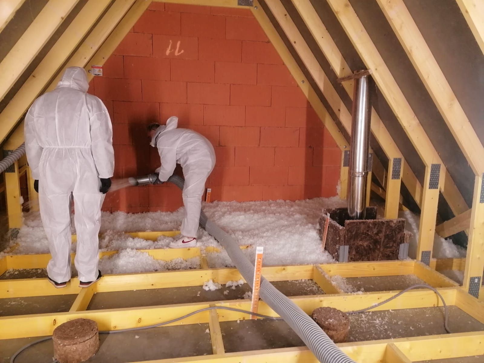 Deux ouvriers en combinaisons de protection isolent un grenier avec des matériaux de remplissage en vrac.