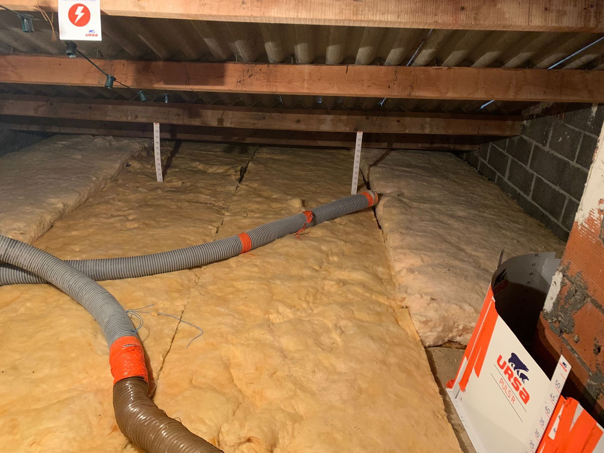 Grenier isolé, avec conduits de ventilation. L'espace sous les poutres en bois est recouvert d'isolant beige.