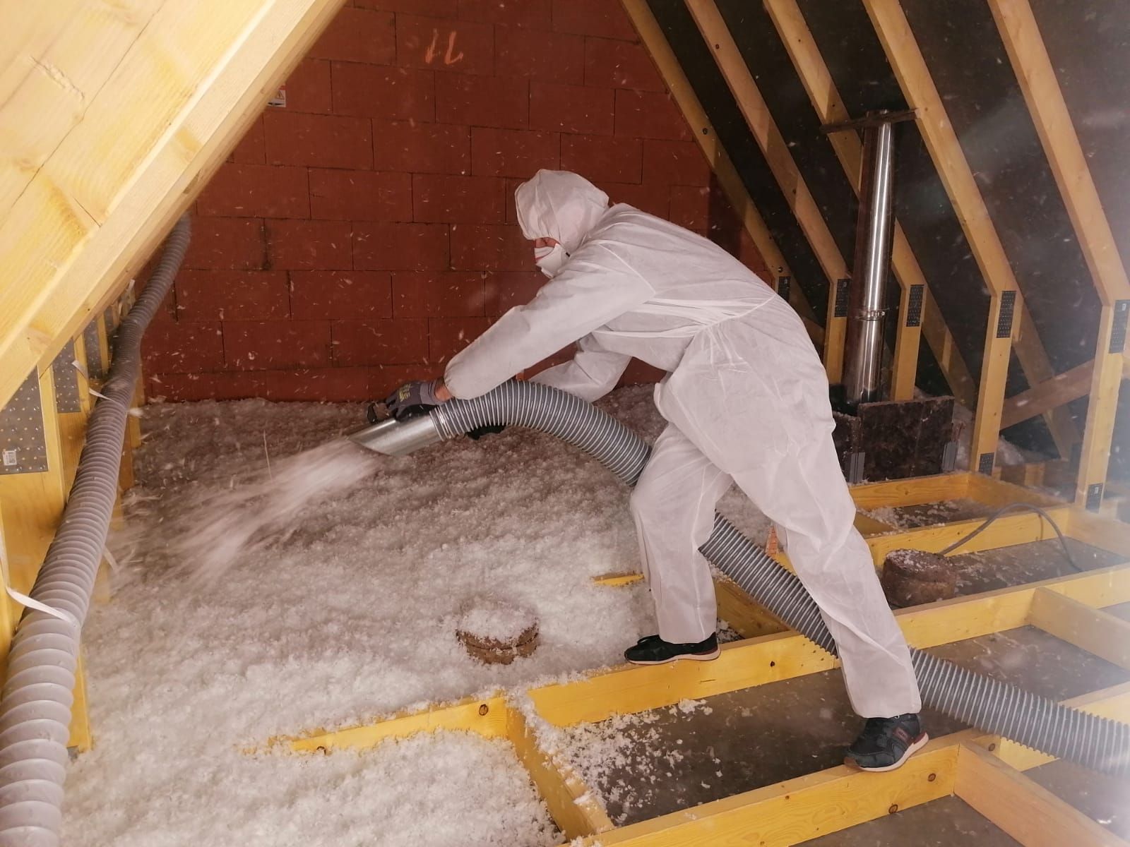 Une personne en combinaison de protection pulvérise de l'isolant dans un grenier.