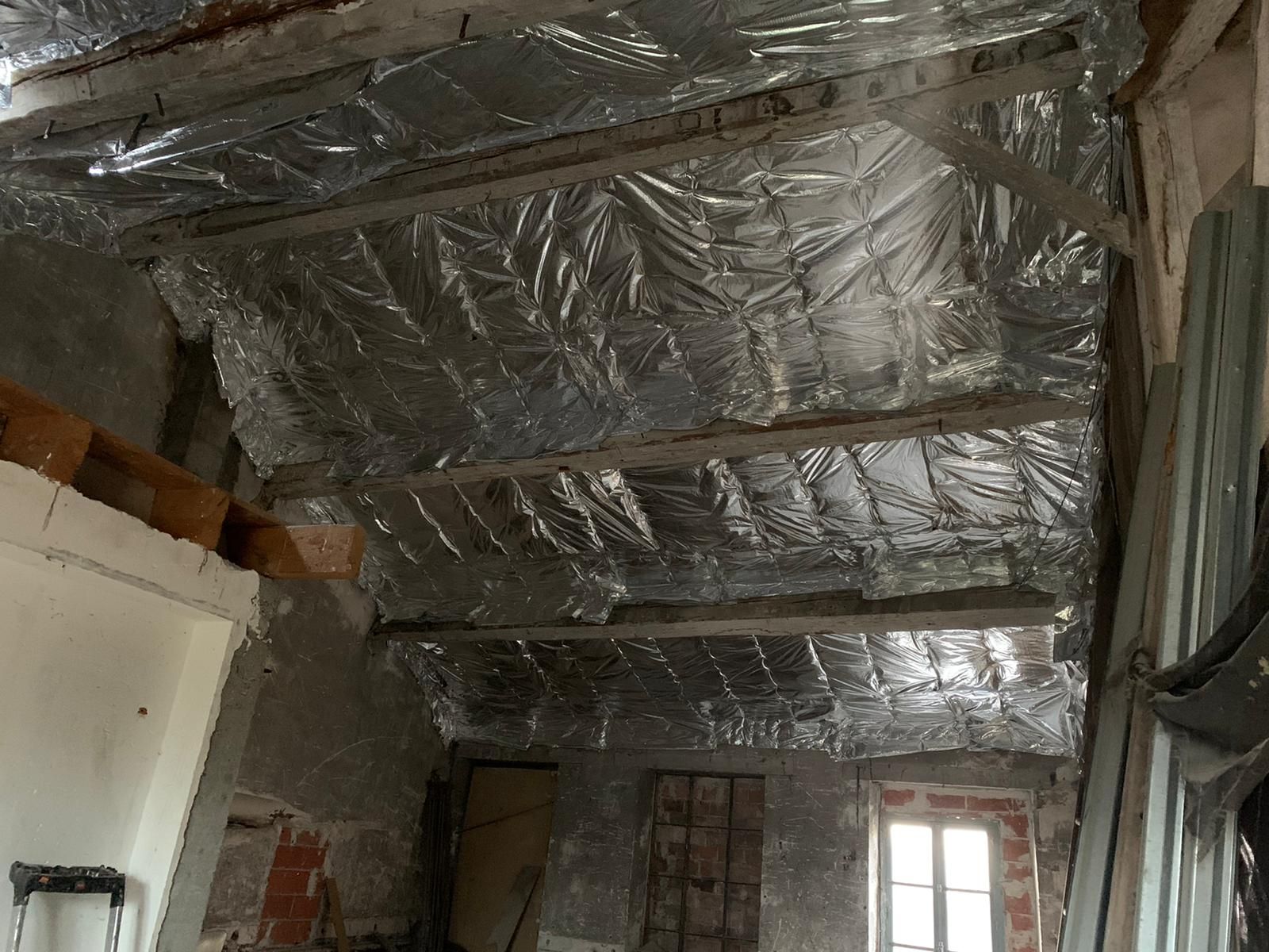 Intérieur du grenier avec poutres en bois apparentes et matériau isolant réfléchissant.