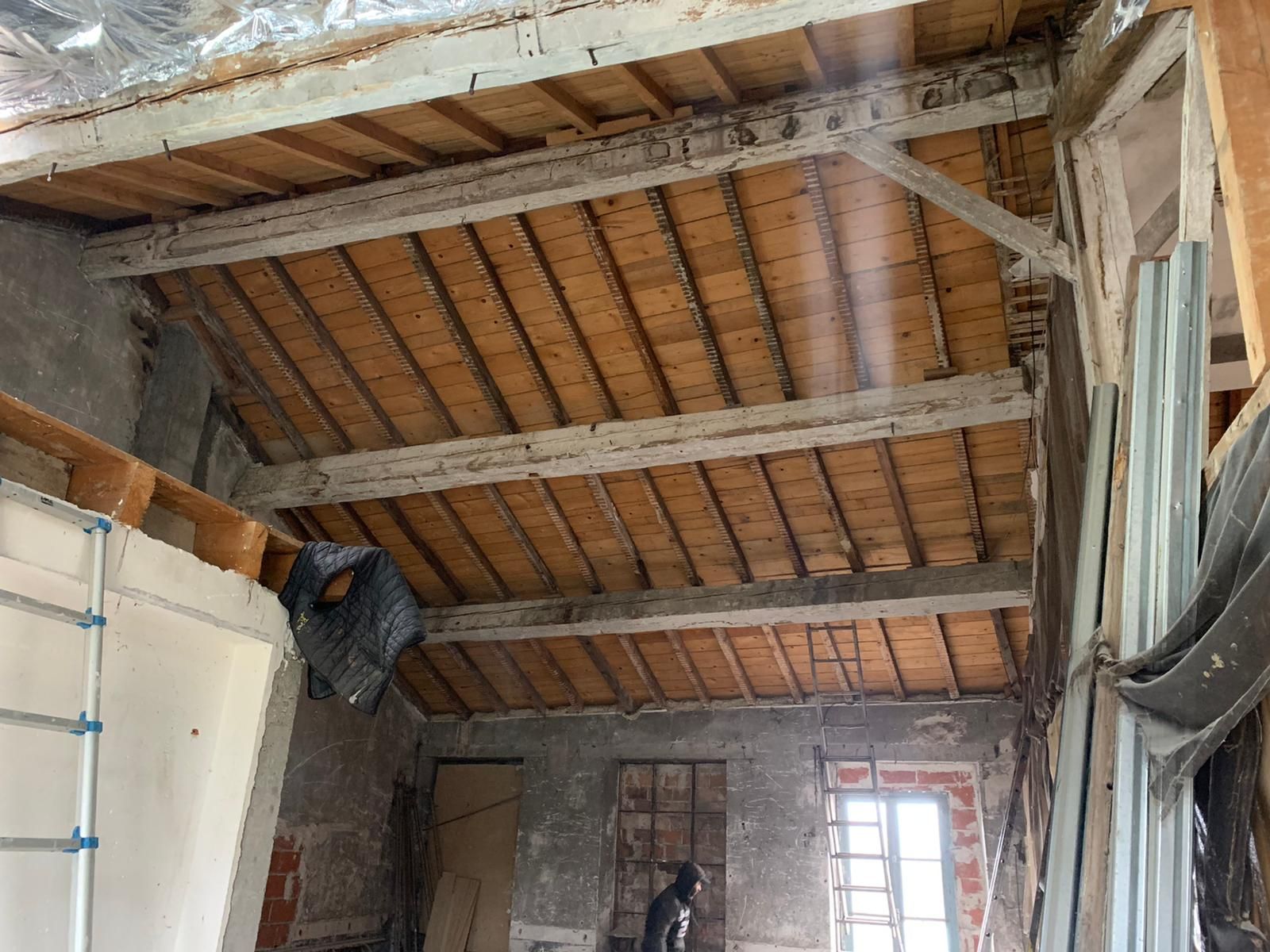 Vue intérieure d'une pièce en construction avec poutres et planches de bois apparentes, et murs non finis.