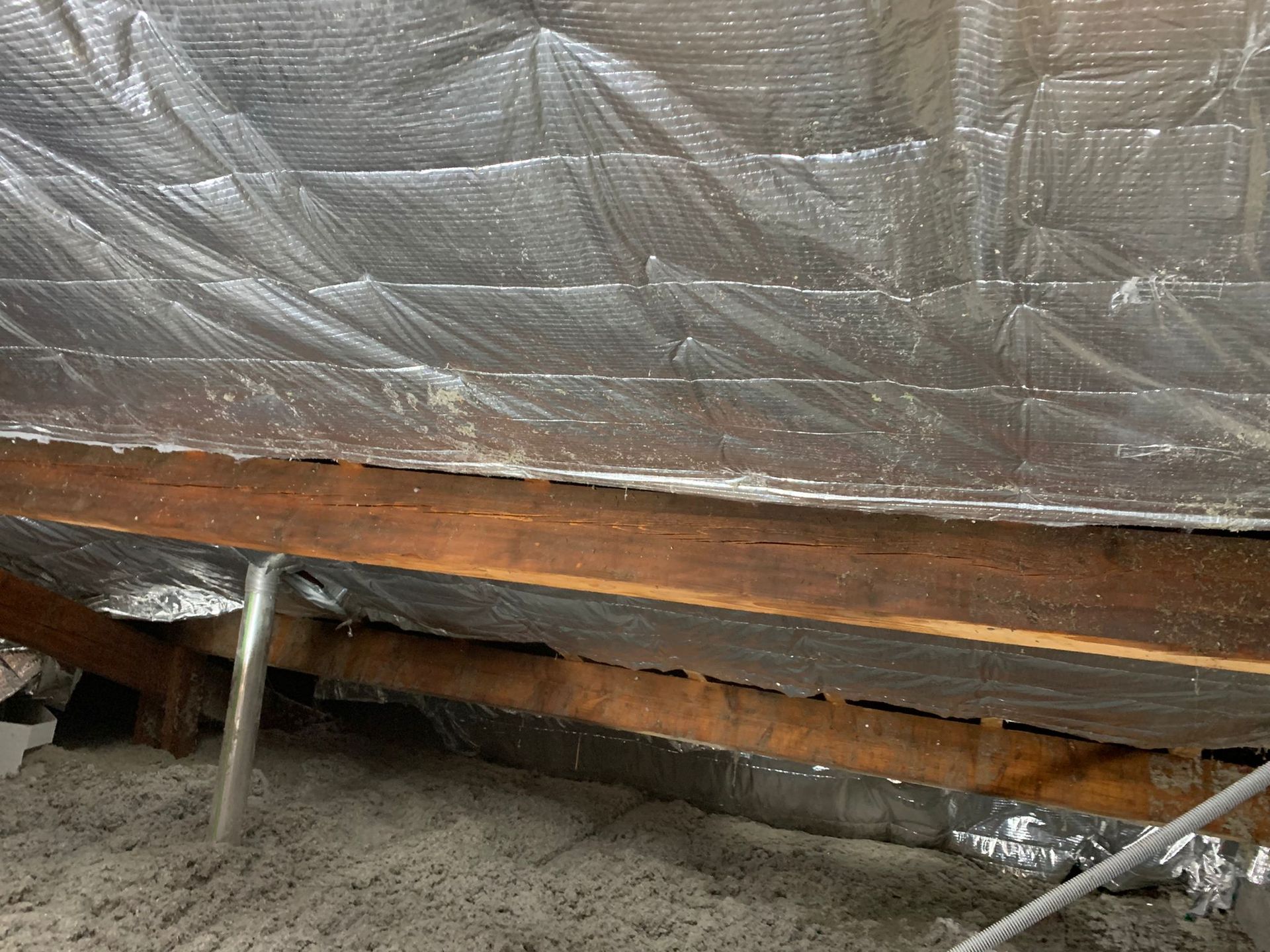 Gros plan sur une poutre en bois et son isolant dans un grenier. L'isolant est argenté et gris.