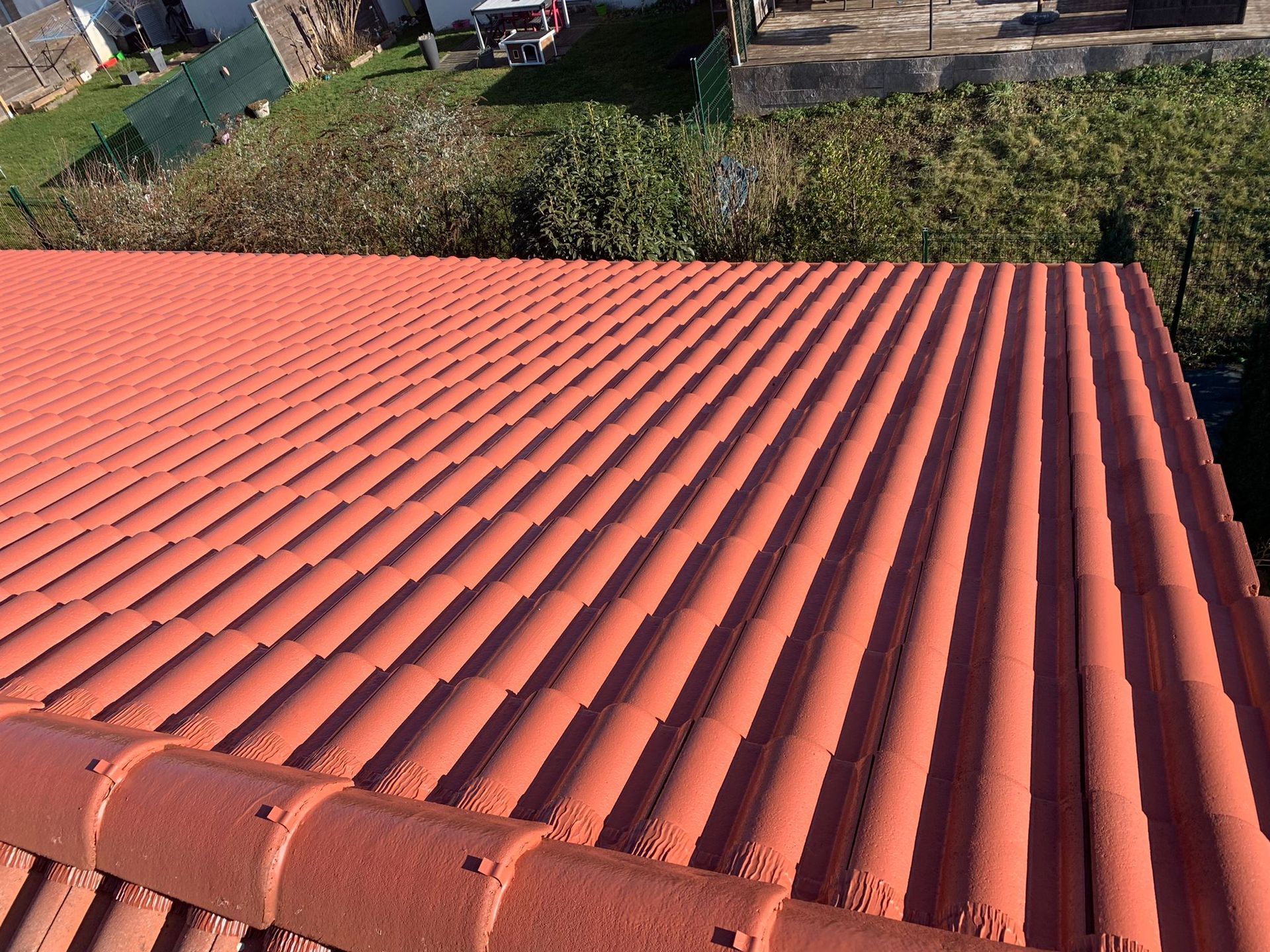 Toit en tôle ondulée rouge offrant une vue sur la verdure et les maisons.