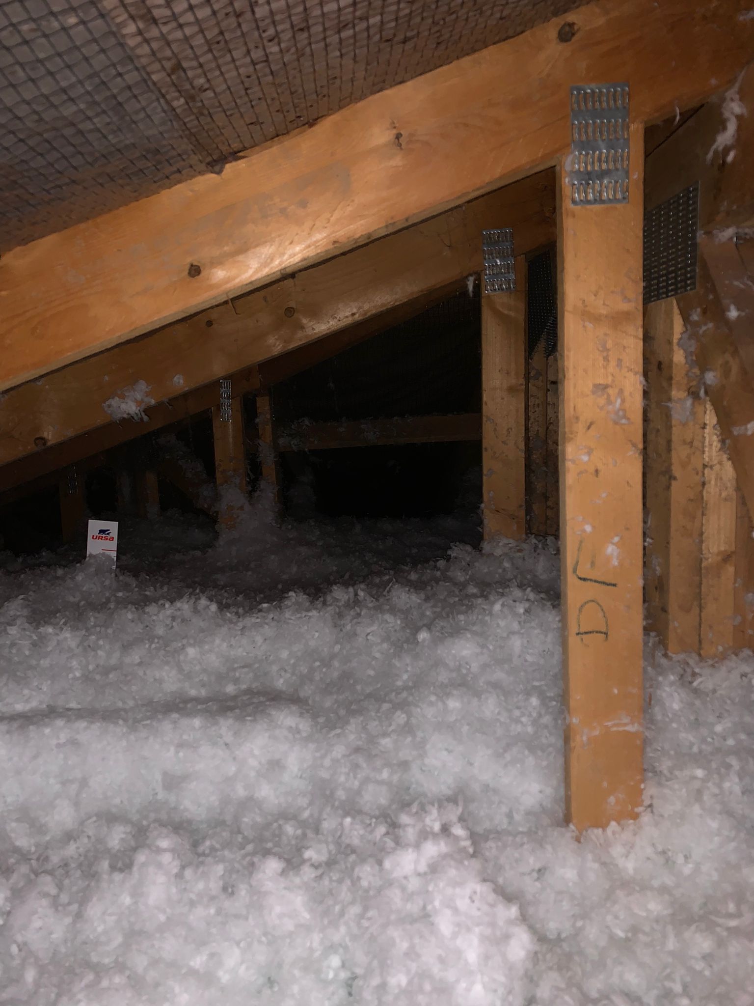 Combles avec poutres en bois et isolation. Les supports verticaux sont fixés aux chevrons par des connecteurs métalliques.