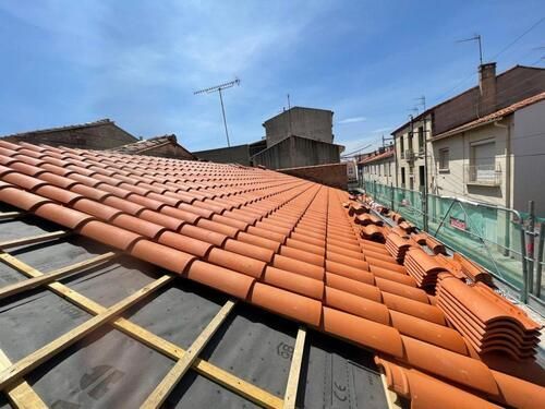 Toiture de tuiles rouges en construction sur un bâtiment avec un ciel bleu en arrière-plan.