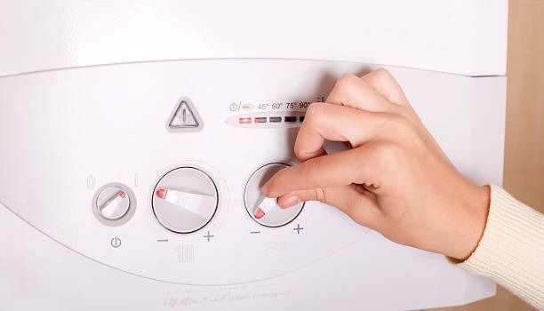 Una persona está ajustando la temperatura de una caldera con el dedo.