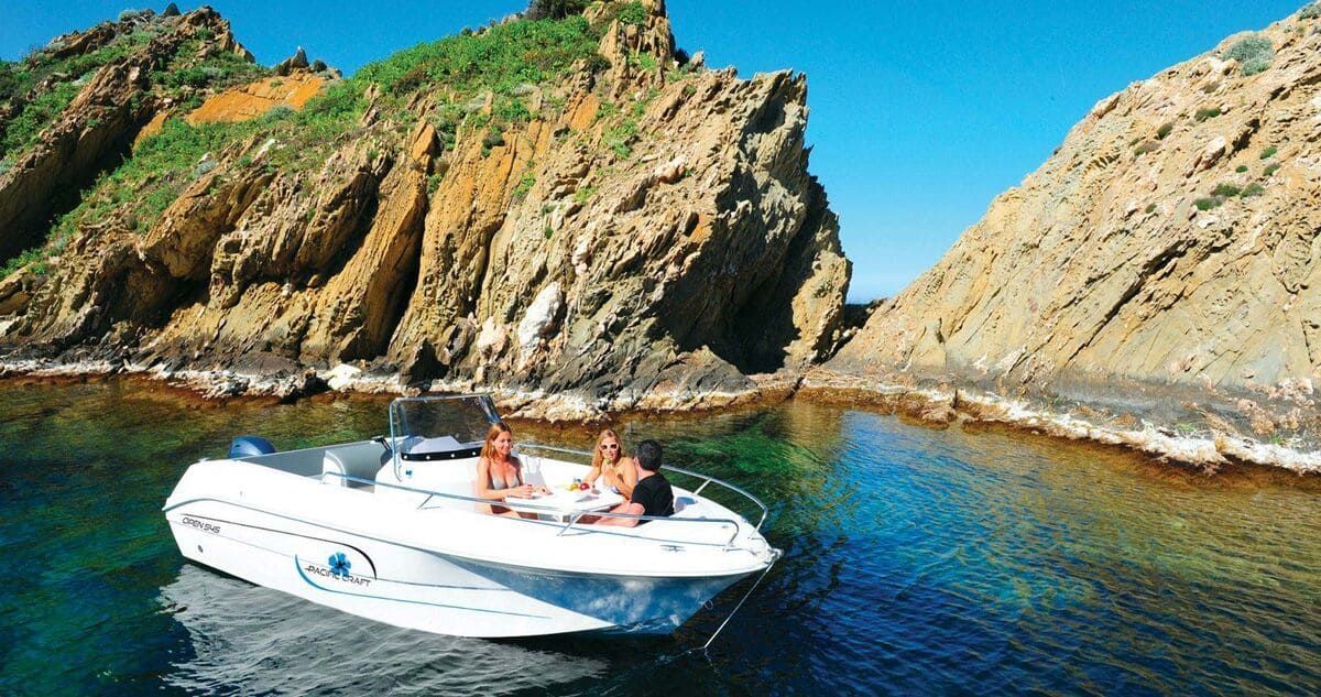 Dos personas están sentadas en un bote en el agua cerca de un acantilado rocoso.