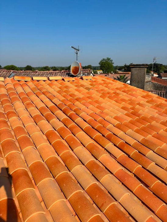 Pose de tuiles orange sur un toit en pente avec des liteaux en bois apparents.