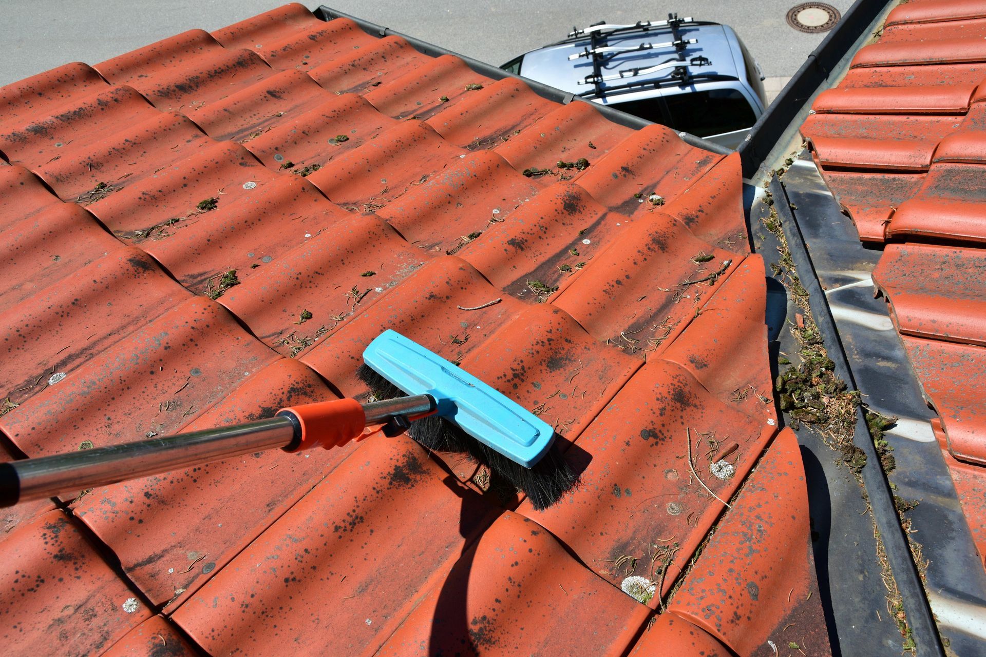 Raclette bleue sur un toit de tuiles rouges près d'une noue et d'une ventilation métallique