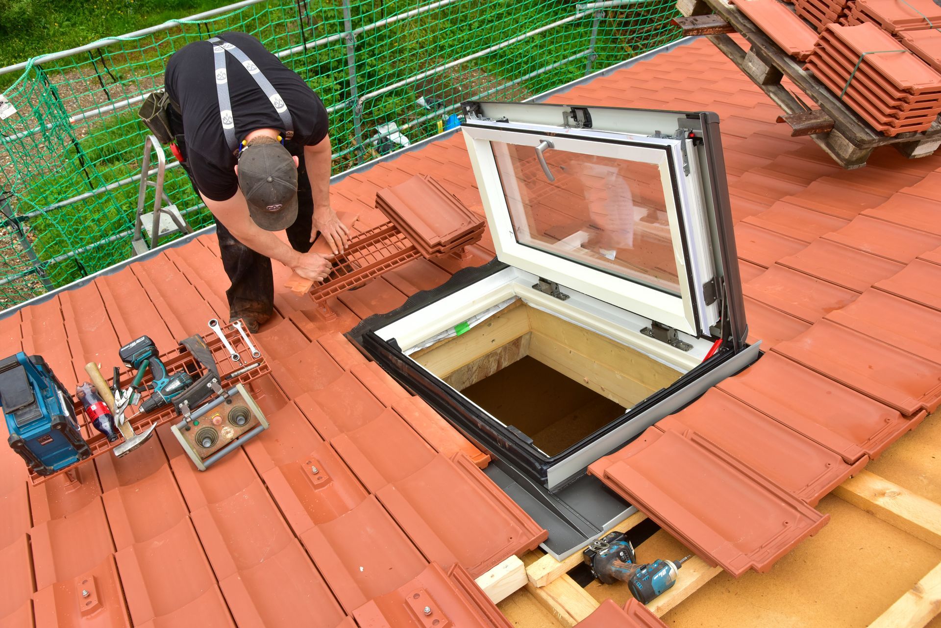 Un ouvrier installe une fenêtre de toit sur un toit de tuiles rouges d'une maison.