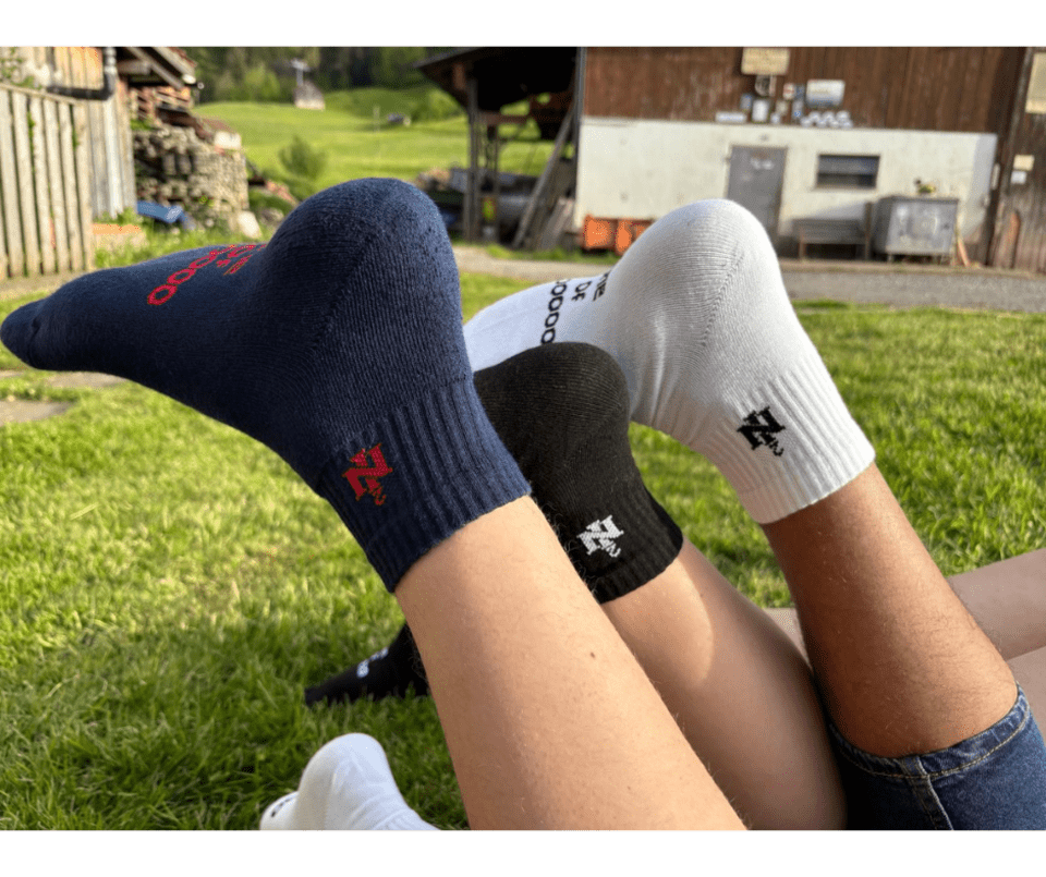 Drei Paar Socken liegen an den Füßen einer Person im Gras.