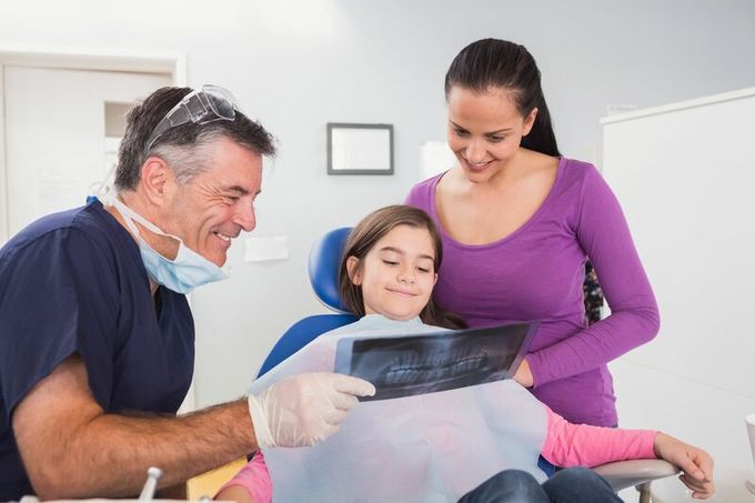 Una niña está sentada en una silla dental mirando una radiografía.