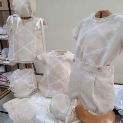 Se exhiben varios conjuntos de bebé de color marrón, incluidos vestidos, camisas, pantalones bombachos y gorros.