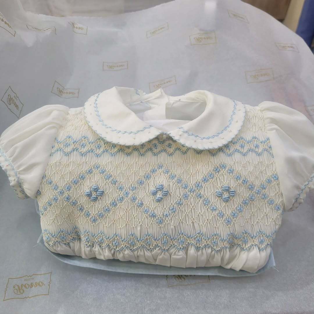 Vestido de bebé bordado en blanco y azul con cuello redondeado.
